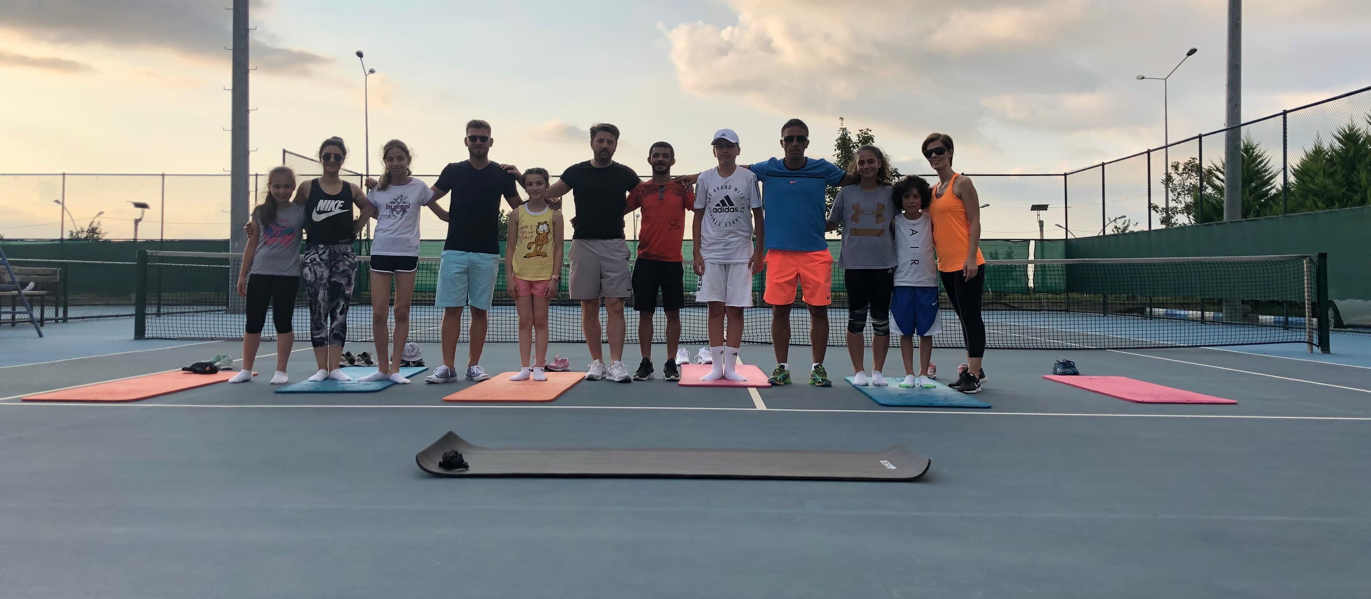 Akşam ışığında kortta sıraya dizilip mat üzerinde ısınma çalışması yapan sporcular